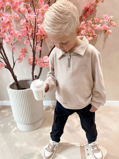 Beige sweater met rits en een geborduurde leeuwen logo en een zwarte cargobroek met zakken voor kinderen