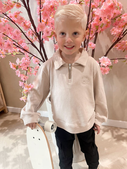 Beige sweater met rits en een geborduurde leeuwen logo en een zwarte cargobroek met zakken voor kinderen