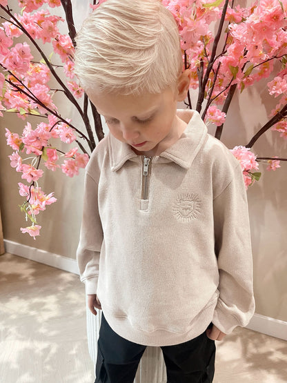 Beige sweater met rits en een geborduurde leeuwen logo en een zwarte cargobroek met zakken voor kinderen