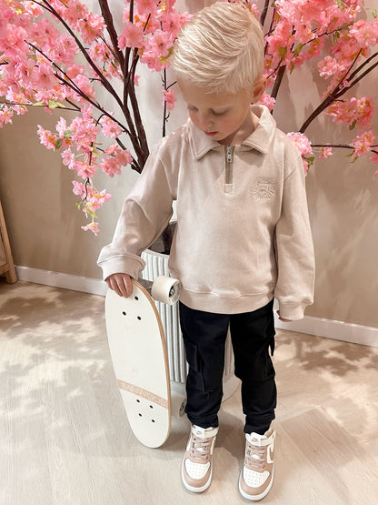 Beige sweater met rits en een geborduurde leeuwen logo en een zwarte cargobroek met zakken voor kinderen