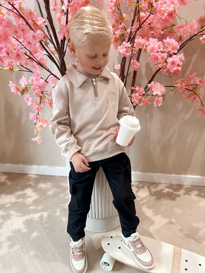 Beige sweater met rits en een geborduurde leeuwen logo en een zwarte cargobroek met zakken voor kinderen